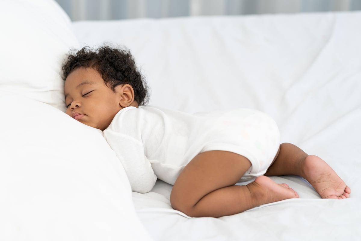 black african american baby sleeping on a white mattress.